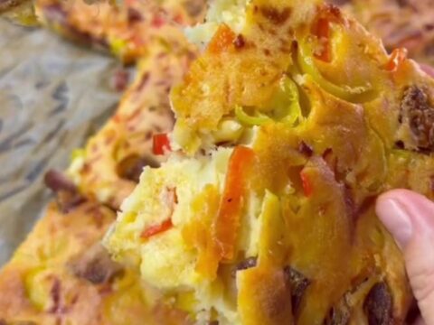 A golden-brown breakfast sheet cake topped with melted cheese and sausage slices, cut into squares.