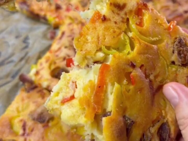 A golden-brown breakfast sheet cake topped with melted cheese and sausage slices, cut into squares.