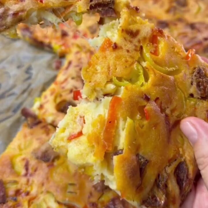 A golden-brown breakfast sheet cake topped with melted cheese and sausage slices, cut into squares.