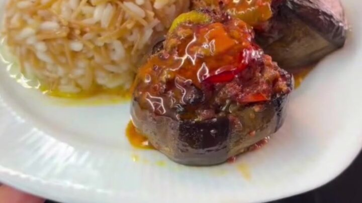 Stuffed eggplant with spiced beef and tomato sauce, garnished with tomato wedges and green peppers.