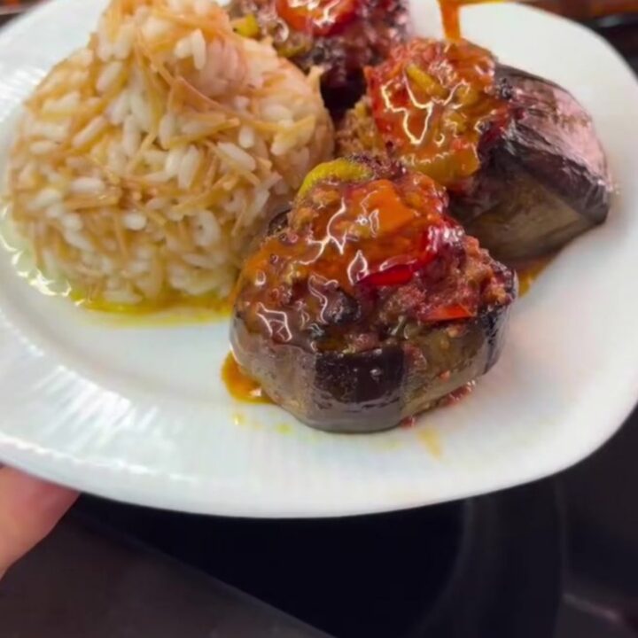 Stuffed eggplant with spiced beef and tomato sauce, garnished with tomato wedges and green peppers.