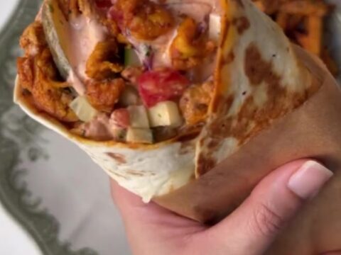 Crispy chicken shawarma wrap sliced in half showing layers of charred chicken, sumac onions, and pickles.