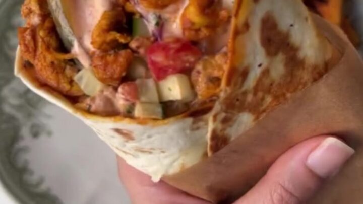 Crispy chicken shawarma wrap sliced in half showing layers of charred chicken, sumac onions, and pickles.