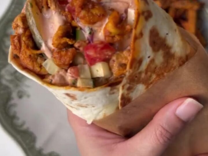 Crispy chicken shawarma wrap sliced in half showing layers of charred chicken, sumac onions, and pickles.