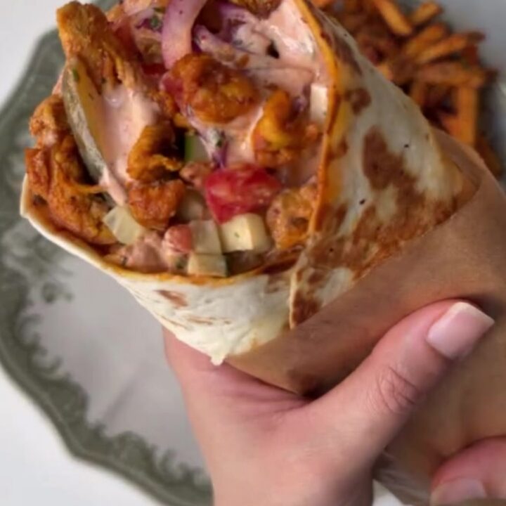 Crispy chicken shawarma wrap sliced in half showing layers of charred chicken, sumac onions, and pickles.