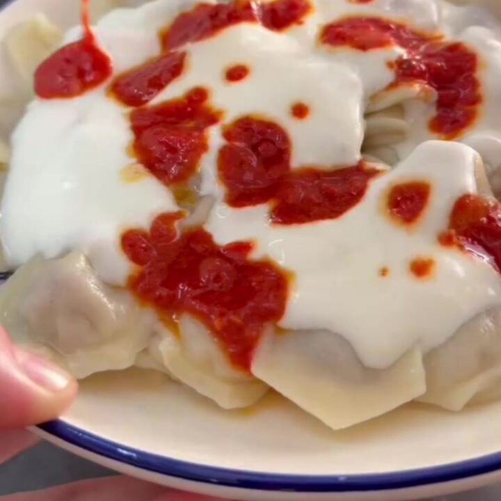 Steaming manti dumplings in a bowl topped with garlic yogurt and sizzling Aleppo pepper butter