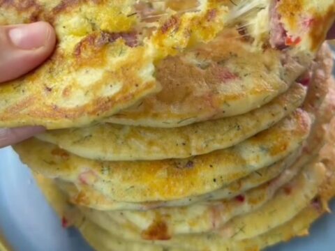 A stack of golden savory pancakes with feta and red pepper on a ceramic plate