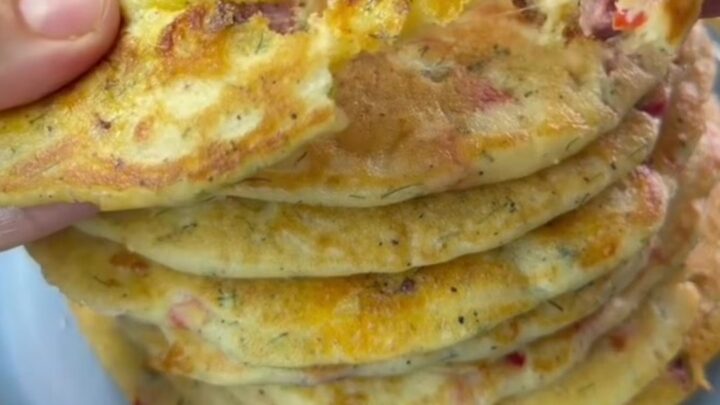 A stack of golden savory pancakes with feta and red pepper on a ceramic plate