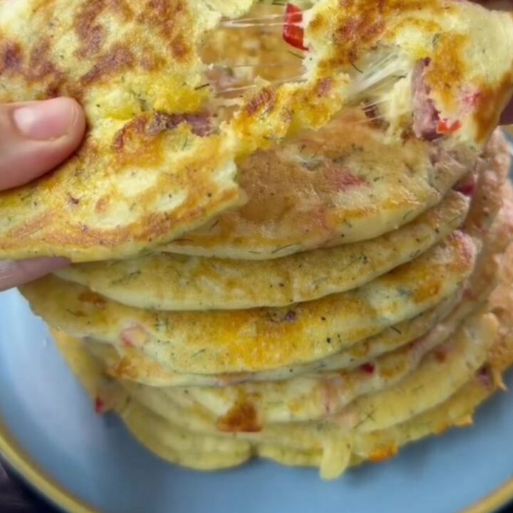 A stack of golden savory pancakes with feta and red pepper on a ceramic plate
