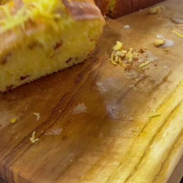 Whole lemon loaf with white glaze on a wooden board, sliced to show yellow crumb