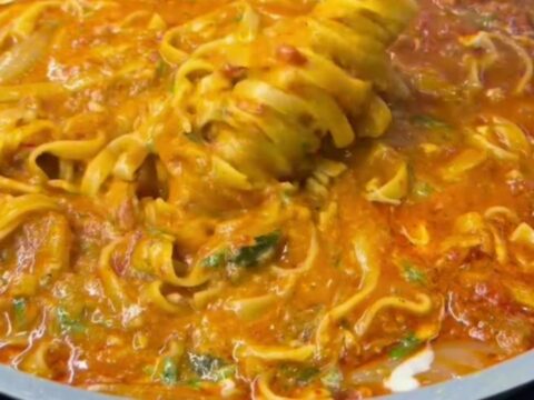 A forkful of tagliatelle with melted cheese and parsley from a skillet