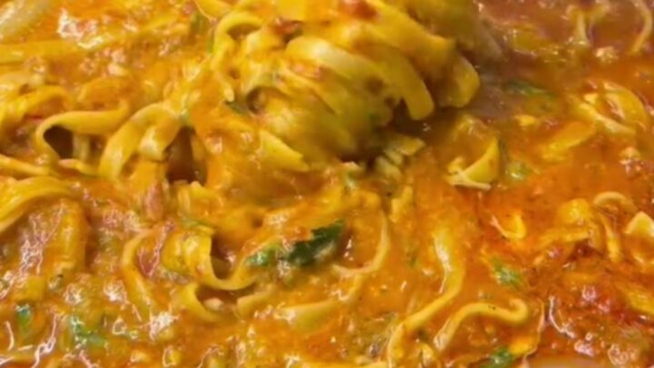 A forkful of tagliatelle with melted cheese and parsley from a skillet