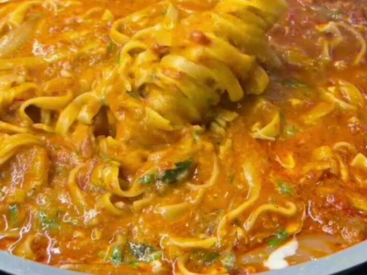 A forkful of tagliatelle with melted cheese and parsley from a skillet