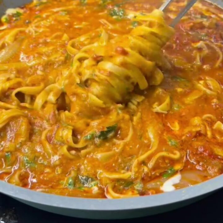 A forkful of tagliatelle with melted cheese and parsley from a skillet