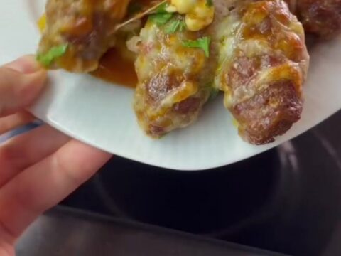 Baking dish with browned cheese topping and meatballs over peppers, melted pull visible