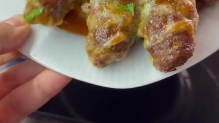 Baking dish with browned cheese topping and meatballs over peppers, melted pull visible