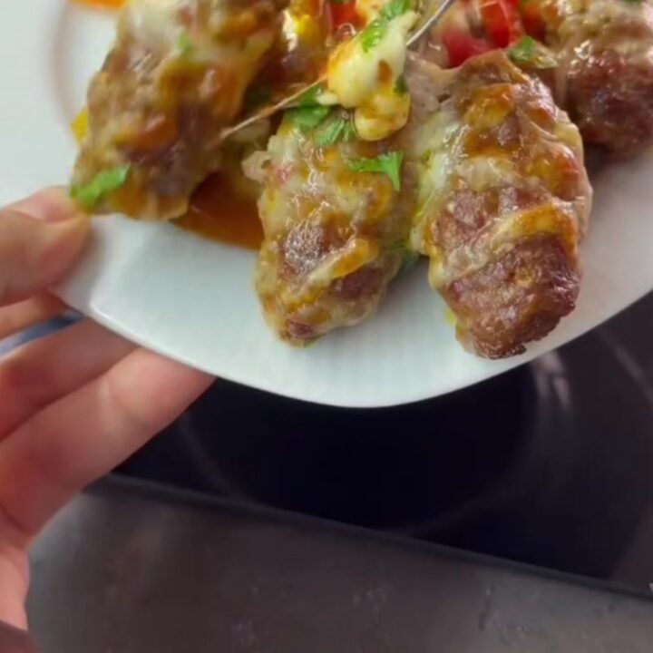 Baking dish with browned cheese topping and meatballs over peppers, melted pull visible