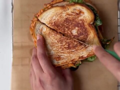 Golden brown sourdough melt with melted cheese oozing out, sliced in half on a cutting board.