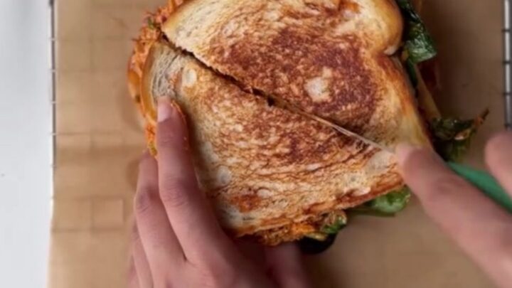 Golden brown sourdough melt with melted cheese oozing out, sliced in half on a cutting board.