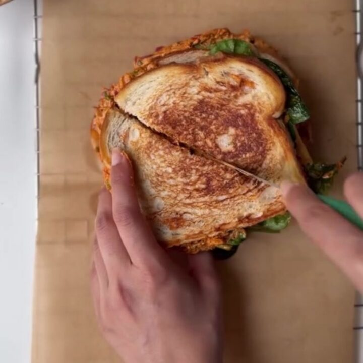 Golden brown sourdough melt with melted cheese oozing out, sliced in half on a cutting board.