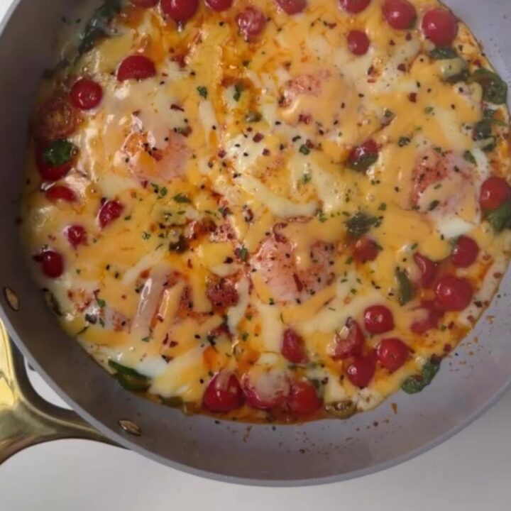 Skillet eggs with blistered tomatoes, jalapeño, and spinach, garnished with nigella seeds and parsley, with a runny yolk.