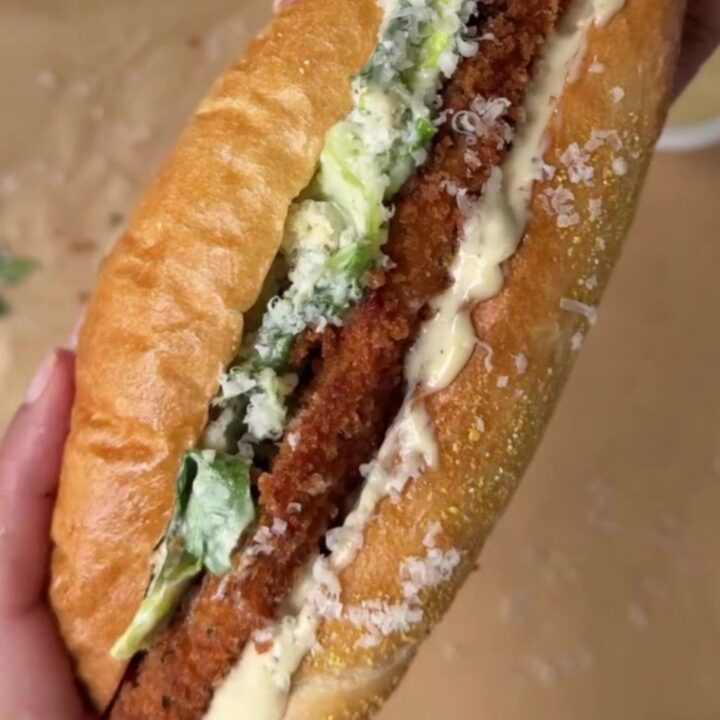 A crispy fried chicken Caesar sandwich on a toasted brioche bun, sliced in half