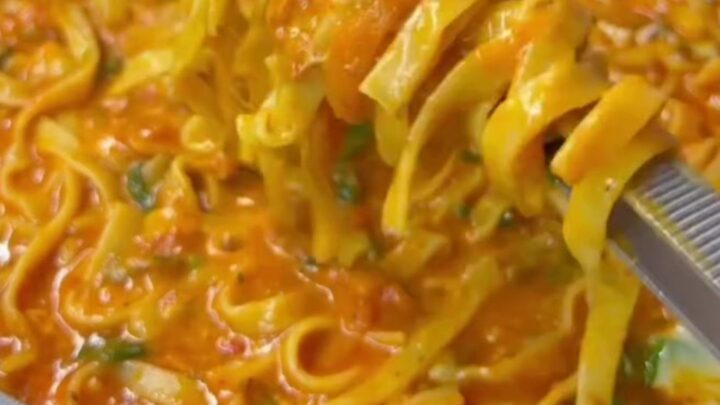 Steamy forkful of pasta with a long, stringy cheese pull, glossy red-orange sauce clinging to ribbons.