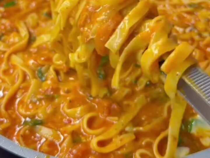 Steamy forkful of pasta with a long, stringy cheese pull, glossy red-orange sauce clinging to ribbons.