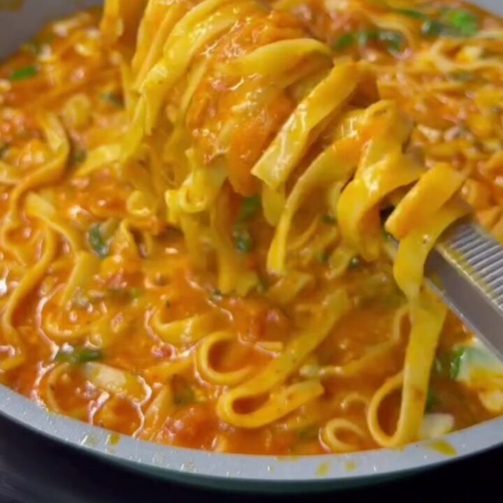 Steamy forkful of pasta with a long, stringy cheese pull, glossy red-orange sauce clinging to ribbons.
