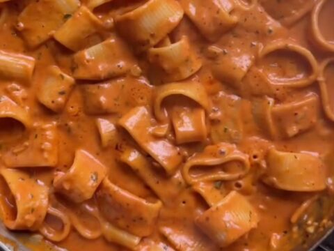 Creamy tomato pasta with melted cheddar and parmesan, topped with fresh basil and cracked pepper in a skillet.