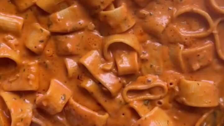Creamy tomato pasta with melted cheddar and parmesan, topped with fresh basil and cracked pepper in a skillet.