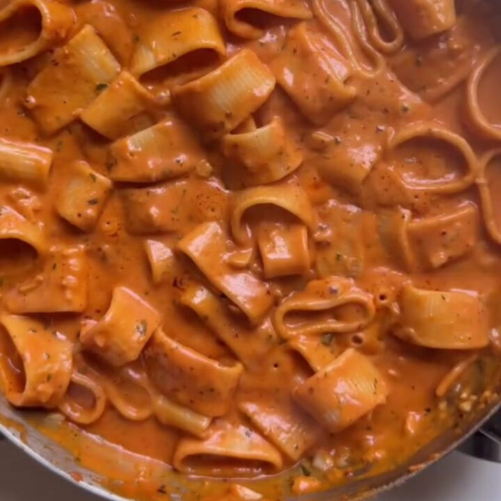 Creamy tomato pasta with melted cheddar and parmesan, topped with fresh basil and cracked pepper in a skillet.