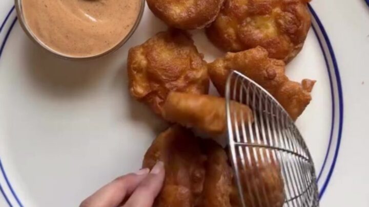 Crispy golden chicken nuggets piled high on checkered paper with a creamy pepper sauce for dipping