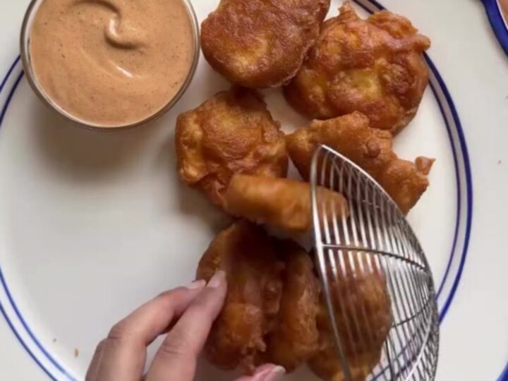 Crispy golden chicken nuggets piled high on checkered paper with a creamy pepper sauce for dipping