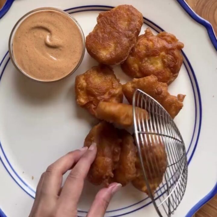 Crispy golden chicken nuggets piled high on checkered paper with a creamy pepper sauce for dipping