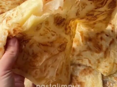 Golden katmer being squeezed, showing crispy buttery layers peeling apart