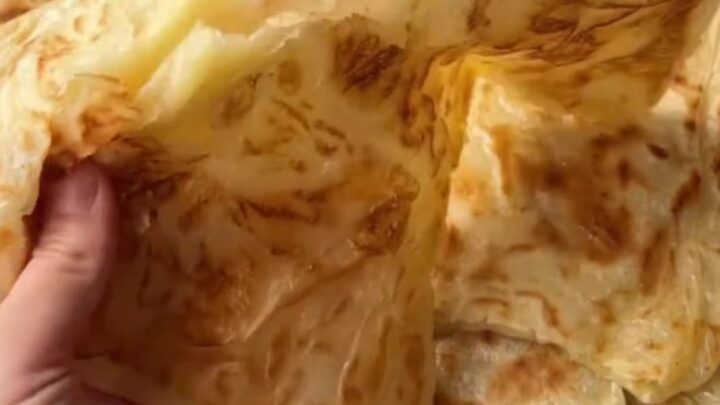 Golden katmer being squeezed, showing crispy buttery layers peeling apart