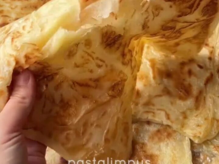 Golden katmer being squeezed, showing crispy buttery layers peeling apart