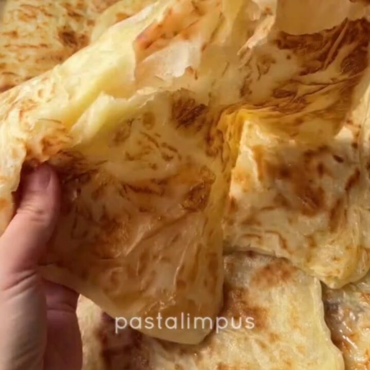 Golden katmer being squeezed, showing crispy buttery layers peeling apart