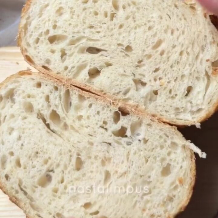 A rustic sourdough loaf with a deep mahogany crust and a crackling, blistered surface, sliced to reveal an open