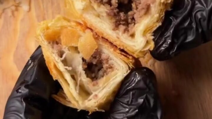Golden blistered börek triangles on a baking sheet, one broken open showing spiced beef filling