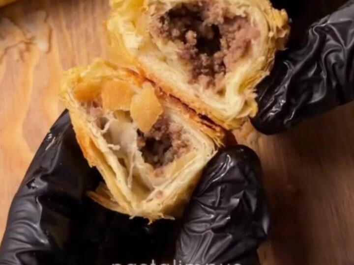 Golden blistered börek triangles on a baking sheet, one broken open showing spiced beef filling
