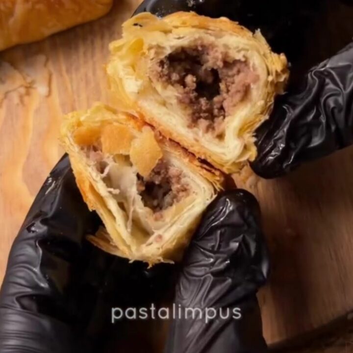 Golden blistered börek triangles on a baking sheet, one broken open showing spiced beef filling