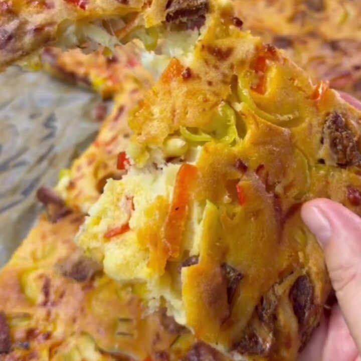 Savory sucuk breakfast sheet cake with melted cheese, sliced into squares on a baking pan