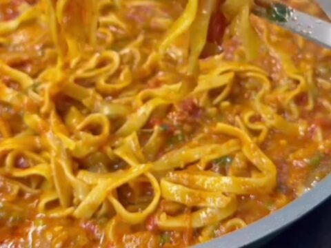 A skillet of tagliatelle pasta with melted mozzarella and parsley, cheese pulling as it's lifted