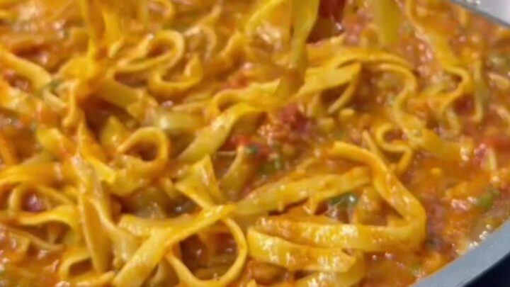 A skillet of tagliatelle pasta with melted mozzarella and parsley, cheese pulling as it's lifted