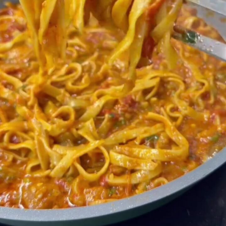 A skillet of tagliatelle pasta with melted mozzarella and parsley, cheese pulling as it's lifted
