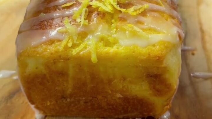 Whole lemon loaf cake with white glaze on a cutting board, slice shown