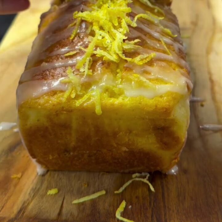 Sliced lemon loaf with white glaze drizzled in zigzags on a wooden cutting board