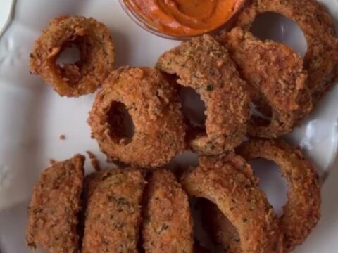 Crispy golden onion rings piled on a platter with a bowl of spicy remoulade sauce